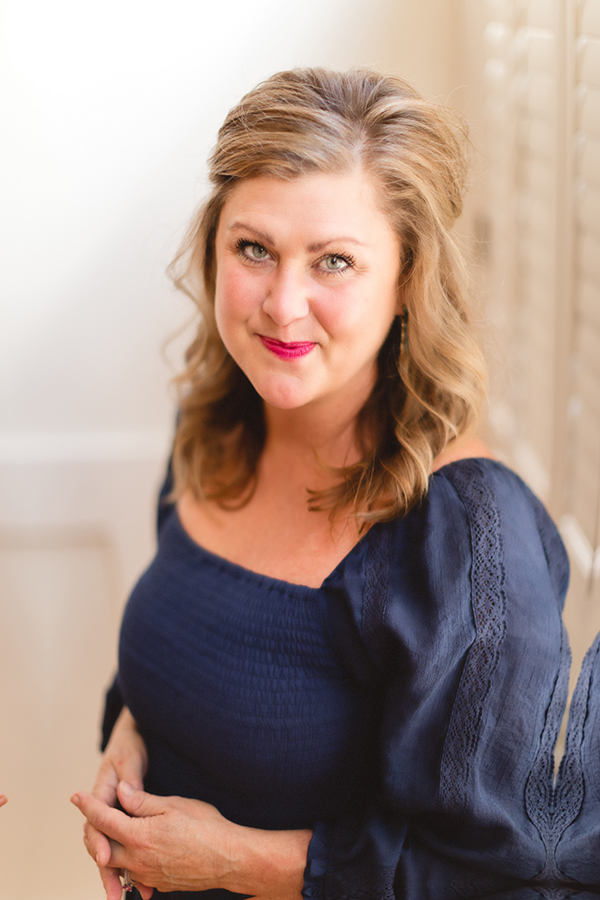Beth Hendricks, Lead Marketing Strategist Woman smiling and looking up, red lipstick, navy dress, hands together